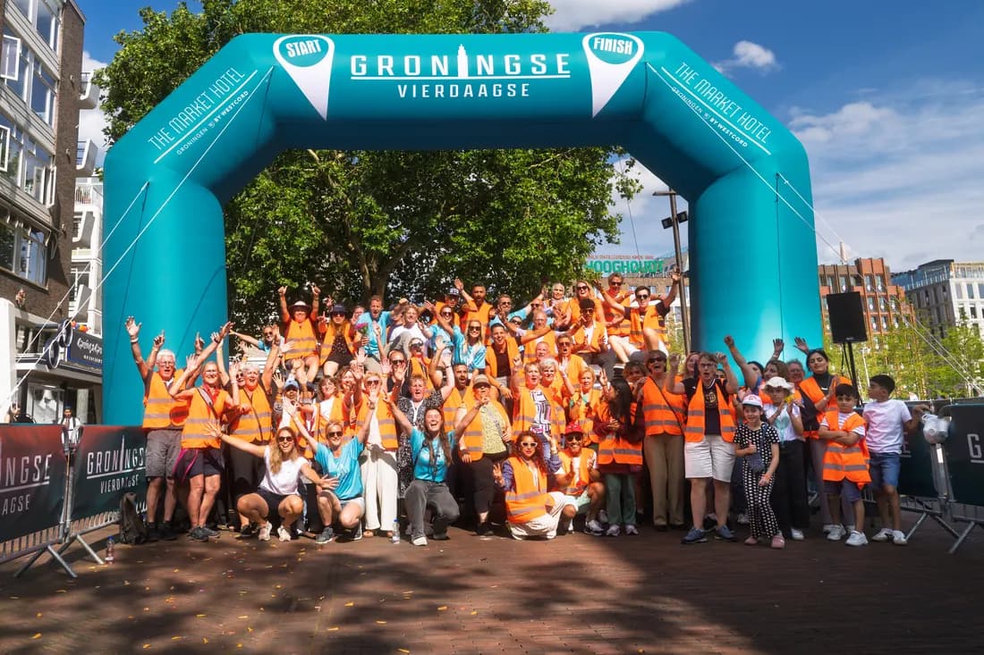 Vrijwilligers en wandelaars onder de start- en finishboog van de Groningse 4daagse